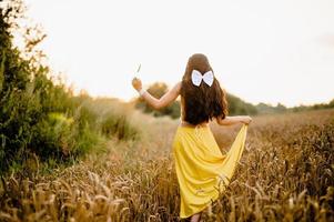 un' ragazza con lungo capelli e un' bianca arco sta nel un' giallo gonna nel un' campo con spighette foto