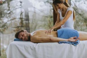 bel giovane uomo sdraiato e con massaggio alla schiena nel salone spa durante la stagione invernale foto