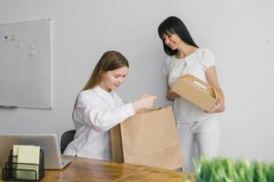 Due ragazze Sorridi e hold lavorazione pacchi, un' Borsa e scatole per cibo nel loro mani foto