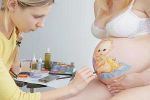 bella trucco artista disegna un' bambino piccolo su il pancia foto