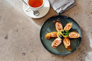 rotoli di magro Pancakes con affumicato salmone, crema formaggio e tazza di tè. delizioso e salutare prima colazione o brunch. superiore Visualizza. foto