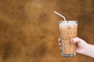 donna mano Tenere il bicchiere ghiacciato caffè su Marrone grungy parete sfondo foto