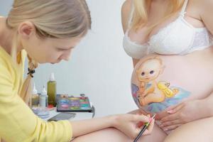 affascinante trucco artista disegna un' bambino piccolo su il pancia foto