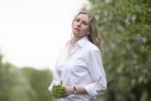 anziano bellissimo donna nel un' bianca camicia in posa nel un' primavera fioritura giardino. foto