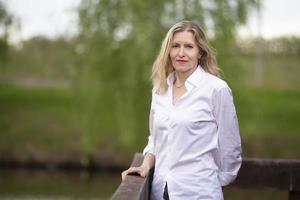 un' bellissimo di mezza età europeo donna. cinquantenne bionda donna nel un' bianca camicia su il sfondo di natura. foto