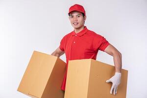 Immagine di un' contento giovane consegna uomo nel rosso berretto vuoto maglietta uniforme in piedi con vuoto Marrone cartone scatola isolato su leggero grigio sfondo studio foto