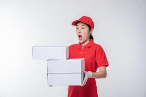 Immagine di giovane consegna uomo nel rosso berretto vuoto maglietta uniforme in piedi con vuoto bianca cartone scatola isolato su leggero grigio sfondo studio foto