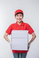 Immagine di giovane consegna uomo nel rosso berretto vuoto maglietta uniforme in piedi con vuoto bianca cartone scatola isolato su leggero grigio sfondo studio foto