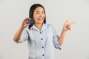 ritratto di positivo giovane asiatico donna mostrando credito carta bene umore stipendio e puntamento dito a a parte isolato su bianca sfondo foto