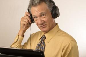 più vecchio uomo ascoltando per musica o un' Podcast indossare testa Telefono su il suo inteligente tavoletta foto