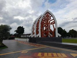 mataram, Indonesia, febbraio 16, 2023. un' cancello con il forma di un' bianca tradizionale Casa tetto e un' rosso stoffa motivo nel sangkaraang parco nel il centro di mataram città foto