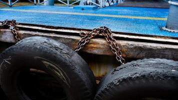 auto pneumatico con metallo catena su vecchio calcestruzzo mare molo, vecchio camion pneumatici a il pier.tire paraurti foto