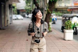 giovane asiatico donna zaino viaggiatore godendo strada culturale Locale posto e Sorridi. viaggiatore controllo su lato strade. foto