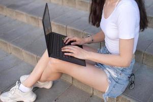 un' ragazza è seduta su il scale, un' il computer portatile su sua giro foto