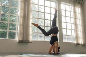 asiatico donna praticante yoga in piedi nel headstand a fitness studio foto