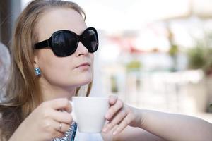 giovane donna che beve caffè indossando occhiali da sole foto