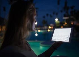 donna che utilizza una tavoletta di notte vicino a una piscina foto