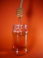 miele vaso con mandrino cucchiaio su arancia sfondo foto
