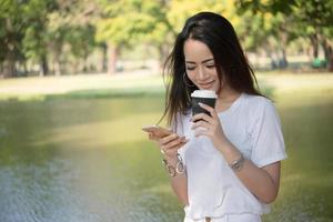 giovane donna che tiene la tazza di caffè durante l'utilizzo di smartphone all'aperto