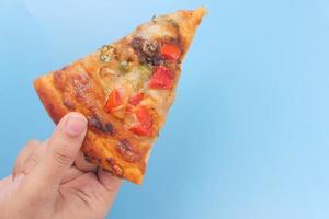 vista dall'alto della mano d'uomo raccogliendo una fetta di pizza su sfondo blu foto