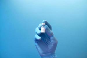 mano in guanti di lattice che tengono il vaccino contro il coronavirus su sfondo blu foto