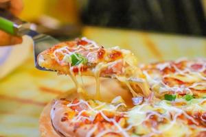 classico Pizza con formaggio su il tavolo nel un' bar su un' di legno In piedi con un' tagliare triangolare pezzo e un' Pizza coltello foto