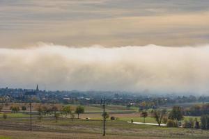 enorme parete di bianca nebbia al di sopra di un' villaggio con i campi foto