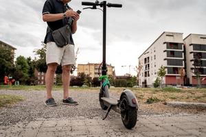pendolare fricchettone uomo con elettrico scooter è utilizzando smartphone nel il periferia foto