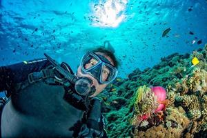divertente autorespiratore tuffatore autoscatto nel blu oceano controluce sole con clown pesce dentro anemone foto