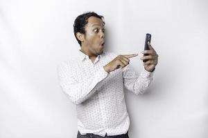 scioccato asiatico uomo indossare un' bianca camicia e Tenere il suo Telefono, isolato di bianca sfondo foto