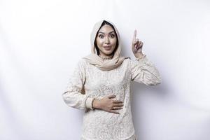 affamato asiatico musulmano donna indossare un' hijab, puntamento su a il copia spazio sopra suo, isolato di un' bianca sfondo foto