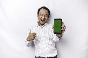 un' ritratto di un' sorridente asiatico uomo indossare un' bianca camicia e mostrando verde schermo su sua Telefono, isolato di bianca sfondo foto