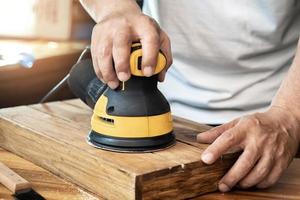 il falegname usa la levigatrice orbitale casuale o la levigatrice palmare lucida il legno in officina, il creatore di fai da te e il concetto di lavorazione del legno. messa a fuoco selettiva foto