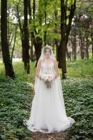 ritratto di un elegante sposa ragazza su un' sentiero nel un' deciduo foresta con un' mazzo foto