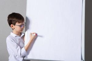 europeo bianca ragazzo in piedi vicino scuola tavola per presentazione. formazione scolastica, infanzia, compiti a casa e scuola concetto. foto