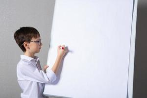 europeo bianca ragazzo in piedi vicino scuola tavola per presentazione. formazione scolastica, infanzia, compiti a casa e scuola concetto. foto