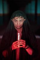 un asiatico uomo con un' trasparente cappuccio coperto nel sangue detiene un' candela nel il suo mano con un' molto pauroso espressione foto