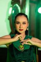 un' bellissimo asiatico donna nel un' verde vestito è in posa con sua mani molto con grazia e ha verde occhi foto