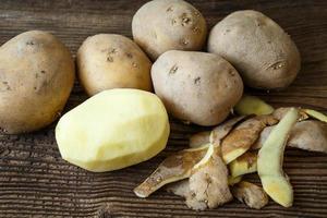 pelato Patata e mucchio di patate su rustico di legno tavolo foto