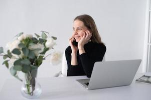 il ragazza lavori nel un' bianca ufficio con un' il computer portatile e fiori su il tavolo foto