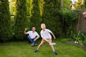 un' allegro papà su il strada supporti il suo figlio. un' ragazzo è giocando badminton nel un' bianca maglietta foto