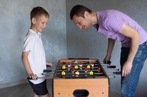 carino ragazzo giocando tavolo calcio con il suo emotivo papà nel il camera foto