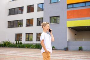 un' bambino detiene un' Telefono nel il suo mani vicino il scuola foto