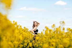 un' ragazza nel un' nero superiore e nero i pantaloni sta nel un' giallo colza campo nel primavera foto