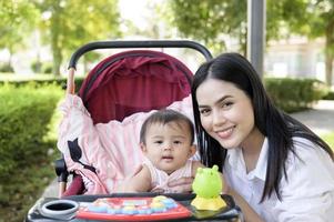 bellissimo mamma con un' bambino ragazza seduta su bambino carrello all'aperto nel luce del sole giorno foto