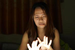 asiatico donne soffrire a partire dal affaticamento degli occhi a partire dal guardare a computer nel Basso luce. orologio film in linea foto