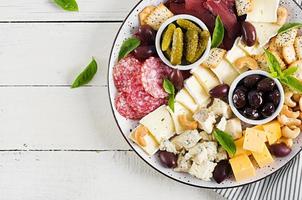 antipasto piatto con bastarma, salame, blu formaggio, noccioline, sottaceti e olive su un' bianca di legno sfondo. superiore Visualizza, alto foto