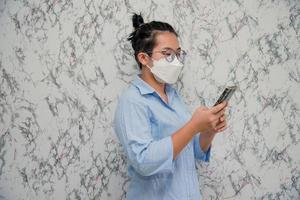 donna mette su un' viso maschera utilizzando smartphone isolato su bianca sfondo, pandemia e sociale distanziamento concetto.covid-19 foto