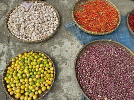 vario verdure pomodori, peperoncino, rosso cipolla, Mais, carota, lime, aglio essere venduto a asiatico tradizionale mercato. colorato verdure su il giro bambù vassoio a tradizionale mercato pavimento foto