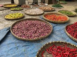 vario verdure pomodori, peperoncino, rosso cipolla, Mais, carota, lime, aglio essere venduto a asiatico tradizionale mercato. colorato verdure su il giro bambù vassoio a tradizionale mercato pavimento foto